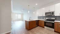 Located at 18000 W 97th St in Lenexa, Kansas, this one-bedroom, one-bathroom residence offers a thoughtfully designed single-floor layout with modern finishes throughout. The open-concept living area seamlessly connects the kitchen, dining, and living spaces, creating an airy and functional environment. Light wood-look flooring runs throughout the main areas, complemented by crown molding and recessed lighting that enhance the clean, contemporary aesthetic.

The kitchen is a standout feature, boasting two-tone cabinetry with white upper cabinets and rich walnut-toned lower cabinets, a gray subway tile backsplash, a peninsula island with a stainless steel sink and pendant lighting, and a full suite of stainless steel appliances including a refrigerator, range, microwave, and dishwasher. A glass-paneled exterior door allows natural light to fill the living area. The bedroom is finished with plush carpet, neutral walls, and a bright window with blinds, offering a comfortable and serene retreat. Four closets provide generous storage throughout the unit. The bathroom features wood-toned cabinetry with a white countertop, a tub-shower combination with large-format tile surround, and wood-look flooring, delivering a polished and cohesive finish.