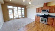 Located on the eighth floor at 1142 Fawcett Ave in Tacoma, WA, Unit 804 is a single-floor residence designed with a clean, functional layout and modern finishes throughout. The open-concept living and kitchen area serves as the heart of the unit, where warm hardwood flooring transitions seamlessly into plush carpeting in the living space. Large, multi-pane windows flood the area with natural light and frame views of the surrounding Tacoma cityscape, with access to an adjoining balcony. The kitchen is well-appointed with rich warm-toned wood cabinetry, granite countertops with a tile backsplash, and a full suite of stainless steel appliances including a gas range, over-the-range microwave, dishwasher, and a side-by-side refrigerator with ice and water dispenser. Recessed and pendant lighting illuminate the space effectively. A long carpeted hallway connects the living areas to the private quarters, lined with wall sconces for a welcoming feel. The bathroom features a wood-toned vanity with a stone-finish countertop, a large mirror, and a tiled shower-tub combination. Throughout the unit, neutral wall tones and consistent trim work create a cohesive, calm ambiance suited for comfortable urban living.