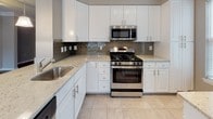 This single-floor residence is thoughtfully designed with a cohesive neutral color palette and quality finishes throughout. The main living area showcases rich, dark hardwood flooring complemented by elegant crown molding and a ceiling fan, creating an inviting atmosphere. Multiple windows dressed with white blinds flood the space with natural light, while a entry door provides direct outdoor access.

The kitchen is well-equipped with crisp white cabinetry, light granite countertops, a gray subway tile backsplash, and stainless steel appliances including a gas range, microwave, and dishwasher. Light tile flooring completes the functional yet stylish cooking space.

The bedrooms feature plush wall-to-wall carpeting in a warm gray tone, with windows offering outdoor views and generous wall space for flexible furniture arrangements. One bedroom includes a door with direct exterior access.

Two bathrooms mirror each other in design, each featuring white cabinetry topped with granite countertops, tile flooring in a neutral stone tone, and framed mirrors. The full bathroom includes a tub-shower combination, while the second bathroom offers a well-lit vanity with overhead lighting.