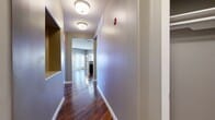 This single-story residence offers a well-organized layout with a cohesive modern design throughout. A hallway finished with rich, dark hardwood-style flooring and flush-mount ceiling fixtures serves as the central spine of the unit, connecting the main living areas. Built-in shelving along the hallway provides convenient storage, while a fire safety device is clearly mounted on the wall.

The living area is generously proportioned, featuring the same hardwood-style flooring, neutral gray walls, a ceiling fan, and a window with blinds that allows natural light to fill the space. Adjacent to it, the kitchen is a functional and stylish focal point, equipped with dark espresso cabinetry, granite countertops, a mosaic tile backsplash, and a full suite of stainless steel appliances.

The bedrooms are carpeted for comfort, each outfitted with a ceiling fan and windows that bring in natural light. The primary bathroom is notably refined, showcasing large-format marble-look tile flooring, a dark-framed vanity with a granite countertop, a soaking tub, and a glass-enclosed walk-in shower with full marble tile surround. A walk-in closet is accessible directly from the bathroom.