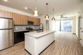 Located at 207 Myrtle Ave in Iowa City, Iowa, this modern single-floor residence offers three bedrooms and two bathrooms with a thoughtfully designed open layout. Light wood-tone flooring runs consistently throughout the home, creating a warm, cohesive aesthetic.

The kitchen serves as a central highlight, featuring a large quartz-topped island with an undermount sink and a sleek matte black faucet. Striking gold pendant lights hang above the island, complementing the two-tone cabinetry — light wood uppers paired with dark lower cabinets. A grey subway tile backsplash and a full suite of stainless steel appliances, including a refrigerator, range, and microwave, complete the space. The kitchen flows seamlessly into the living area, which benefits from large windows that allow ample natural light and includes a ceiling fan.

The bedrooms are clean and functional, each featuring ceiling fans, natural light from windows, and neutral white walls. One bedroom includes an adjacent walk-in closet with wire shelving. Both bathrooms are finished in a modern style, with quartz-topped dark vanities, matte black hardware, and tub-shower combinations clad in large-format marble-look tile. The hallway connects all rooms efficiently, maintaining an organized and practical floor plan throughout.