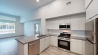 Located at 505 W Crowther Ave in Placentia, CA, this thoughtfully designed three-bedroom, two-bathroom residence offers a clean, contemporary aesthetic throughout its single-story layout. The open-concept kitchen anchors the living space with striking soaring ceilings that amplify the sense of volume. White flat-panel cabinetry lines the walls, complemented by gray quartz countertops, a stainless steel gas range, over-the-range microwave, dishwasher, and refrigerator. Light wood-tone flooring runs through the main living areas, adding warmth to the modern palette. The bedrooms are carpeted and bathed in natural light through large windows with elevated transom panels, enhancing the airy feel. The primary bedroom offers a comfortable, well-proportioned retreat. Both bathrooms mirror the home's modern design language, featuring white cabinetry, quartz countertops, undermount sinks, and tub-shower combinations with white tile surrounds. Two closets provide practical storage, including a walk-in style closet with wire shelving. The unit's neutral color scheme, recessed lighting, and consistent finishes create a cohesive and inviting atmosphere throughout.