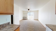 This single-floor unit offers a practical and straightforward layout connecting the main living areas seamlessly. The living room is a comfortably sized, carpeted space bathed in natural light from a sliding glass door that opens to an outdoor area. A ceiling fan with a built-in light fixture provides overhead circulation and lighting, while a wall-mounted HVAC unit ensures climate control. Neutral-toned walls and warm wood baseboards carry throughout the unit, creating a cohesive, understated aesthetic.

The galley-style kitchen runs parallel walls of warm oak cabinetry paired with granite-look countertops, offering generous storage and prep space. White appliances, including an electric range, microwave, dishwasher, and refrigerator, are included. Light hardwood-style flooring grounds the kitchen and entry areas.

The bedroom is a well-proportioned, carpeted room with a large window fitted with vertical blinds, allowing ample natural light. A doorway leads to an adjacent hallway with closet access.

The bathroom features oak cabinetry with a white countertop, a mirrored medicine cabinet, a vanity light bar, a toilet, and a bathtub, all finished with light vinyl flooring. The overall ambiance of the unit is clean, functional, and move-in ready.