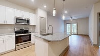 This thoughtfully designed single-floor residence in Indian Land, South Carolina, offers a clean, modern aesthetic with an open-concept layout that maximizes every inch of its well-utilized floor plan. Light wood-look flooring flows consistently throughout the home, creating a seamless and cohesive feel from room to room.

The kitchen serves as the centerpiece of the living area, anchored by a granite-topped island with an undermount sink and pendant lighting overhead. White shaker-style cabinetry provides ample storage, while a full suite of stainless steel appliances — including a refrigerator, range, microwave, and dishwasher — adds a contemporary, functional edge. A tile backsplash completes the polished look.

The open living area is bright and airy, featuring a ceiling fan, recessed lighting, and French doors that invite natural light and provide outdoor access. The spacious primary bedroom offers a ceiling fan, a large window with exterior views, and direct access to a dedicated walk-in closet outfitted with wire shelving for organized storage.

The bathroom features a white vanity with granite countertops, brushed nickel hardware, a large mirror, and matching flooring. A hallway connects all rooms, ensuring a practical and intuitive flow throughout this well-finished home.