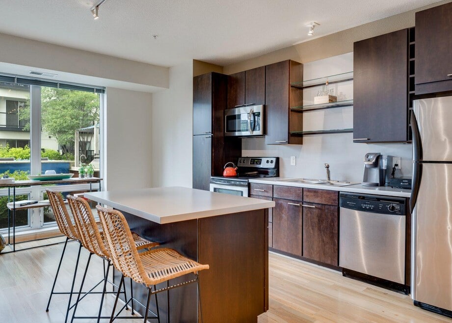 Modern kitchen with island and bar stools, stainless steel appliances, and large window with view.