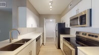 Located at 9131 SW 122nd Ave in Miami's Kendall neighborhood, this single-story residence showcases a thoughtfully designed open-concept layout with notable architectural details. The living area immediately impresses with dramatically vaulted ceilings that lend a sense of spaciousness, complemented by wood-look flooring in a warm gray tone. A peninsula with a built-in sink and white quartz-style countertop connects the living space to the kitchen, creating a functional and visually cohesive flow. Sliding vertical blinds allow natural light to filter in from an outdoor-facing door.

The galley-style kitchen is well-appointed with white shaker cabinetry, light countertops, a subway tile backsplash, and a full suite of stainless steel appliances including a refrigerator, electric range, microwave, and dishwasher. Louvered bifold doors lead to an in-unit laundry area. A hallway connects to the bedrooms, each featuring light wood-look flooring, neutral warm-gray walls, louvered closet doors with built-in shelving, and windows overlooking greenery. Two bathrooms serve the unit, one featuring a tub-shower combination with white tile surround, and the other a half-bath configuration—both finished with white vanities and light countertops.