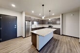 Located at 3401 E Washington Ave in Madison, WI, this well-appointed 3-bedroom, 2-bathroom residence offers a thoughtfully designed single-floor layout with modern finishes throughout. The open-concept kitchen and living area serves as the heart of the home, anchored by a large center island with a striking granite countertop and dark cabinetry. Pendant lighting illuminates the workspace, while a classic white subway tile backsplash and full suite of stainless steel appliances complete the kitchen. The living area extends naturally from the kitchen, featuring durable hardwood-style flooring, a ceiling fan, and sliding glass doors that open to a private balcony with outdoor views. The three bedrooms are carpeted and each includes a ceiling fan, ample natural light from large windows, and generous closet space — six closets in total across the unit. The primary bedroom offers a comfortable, well-proportioned retreat. Two bathrooms serve the residence: one features a soaking tub with shower combination, while the other offers a walk-in shower, both finished with wood-style flooring and dark vanity cabinetry. An in-unit laundry area adds everyday convenience. The overall aesthetic is clean, contemporary, and functional.