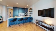Located at 1314 Franklin St in downtown Oakland, this thoughtfully designed single-floor residence combines contemporary finishes with striking urban views. Herringbone-patterned hardwood flooring flows throughout the space, providing a warm and cohesive foundation that connects each area seamlessly.

The open-concept kitchen is a standout feature, showcasing bold teal cabinetry that extends to the ceiling, complemented by a white quartz waterfall island with seating for multiple guests. Stainless steel appliances and open wall shelving complete the functional yet stylish space, which flows naturally into the living area.

The living room is anchored by floor-to-ceiling windows that frame sweeping panoramic views of the Oakland skyline and beyond, flooding the interior with abundant natural light. A dedicated study or flex space offers a tall wood-and-metal open bookshelf, providing a quiet retreat adjacent to the main living area.

The bedroom continues the floor-to-ceiling window theme, offering spectacular city views as a backdrop. The bathroom features large-format marble-style tile, a glass-enclosed walk-in shower, and a navy floating vanity topped with a backlit mirror.

A dedicated in-unit laundry area and a well-lit entry corridor with recessed lighting round out this polished, modern residence.