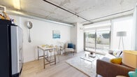 Located at 1522 Gordon St in the heart of Hollywood, Los Angeles, this single-floor unit showcases a compelling blend of industrial and modern design. The exposed concrete ceiling with visible ductwork sets a striking architectural tone throughout, complemented by light hardwood flooring that adds warmth to the open-plan layout.

The living area is bright and airy, anchored by large sliding glass doors that open directly onto a private outdoor patio, allowing natural light to pour into the space and creating a seamless indoor-outdoor connection. A raw concrete accent column adds an authentic industrial character to the living room.

The kitchen is efficiently designed with light wood cabinetry, stainless steel appliances including a full-size refrigerator, electric range, and dishwasher, along with ample counter space for meal preparation.

The bedroom is a private retreat, partially separated by a partial-height wall partition that maintains an open, loft-like feel while providing a defined sleeping area. Exposed concrete ceilings continue here, reinforcing the cohesive industrial aesthetic.

The bathroom features large-format tile flooring, a wood-accented vanity with an integrated sink, and a clean, minimalist design.

Overall, this space offers a sophisticated urban living experience with thoughtful design details, abundant natural light, and direct outdoor access.