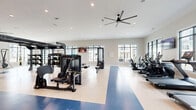 Located at 4000 Galantis Dr in Morehead City, NC, this comprehensive fitness center spans a generously sized single-floor layout designed to accommodate a wide range of workout styles and fitness goals. The facility is divided into two primary areas, each thoughtfully appointed to deliver a complete exercise experience.

The main gym floor features durable two-tone flooring with a bold blue accent stripe, lending a clean, athletic aesthetic to the space. Large black-framed windows line the walls, flooding the interior with natural light and offering views of the surrounding community. Overhead, large ceiling fans circulate air throughout the open floor plan, complemented by recessed lighting. This area houses an extensive array of TRX suspension systems, cable machines, weight benches, strength equipment, punching bags, and a full row of True-brand cardio machines including treadmills, ellipticals, and steppers. Wall-mounted televisions provide entertainment throughout.

A separate studio space features warm hardwood-style flooring and stylish textured accent walls. This room is equipped with stationary spin bikes, BOSU balance trainers, stability balls, resistance bands, rowing machines, and an air bike, making it ideal for group classes or individual functional training. A barn-style glass door and full-length mirror add refined architectural detail to this versatile studio.