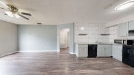 Located at 400 Rosewood Ave in Boerne, TX, this single-story 2-bedroom, 1-bathroom home offers a thoughtfully updated interior with a clean, modern aesthetic. The open-concept kitchen and living area serves as the heart of the home, featuring durable wood-look flooring, soft blue-gray walls, and a textured ceiling. The kitchen is well-appointed with sage-toned shaker cabinets, granite countertops, a striking floor-to-ceiling marble-style tile backsplash, and black appliances including a range, dishwasher, and refrigerator. Floating shelves add a contemporary touch above the counter space.

Both bedrooms are carpeted and equipped with ceiling fans and windows that invite natural light. The primary bedroom is a comfortable size with access to a closet, while the second bedroom also features a window with outdoor views of surrounding trees. A hallway connects the living spaces to the bedrooms and bathroom.

The bathroom is finished with a granite-topped vanity, wood-look flooring, and a walk-in shower enclosed by sliding glass doors with large-format gray tile surround. Throughout the home, consistent finishes and neutral tones create a cohesive and move-in-ready feel.