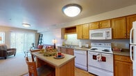 This single-floor residence offers a thoughtfully designed layout that balances functionality and comfort throughout its key living areas. The kitchen is a standout feature, outfitted with warm honey-toned wood cabinetry that extends to the ceiling for generous storage, a double stainless steel sink, and a full suite of white appliances including a refrigerator, electric range, built-in microwave, and dishwasher. A central kitchen island provides additional workspace and casual dining. Light hardwood flooring runs through the kitchen, lending warmth and continuity to the space.

The bedroom is a tranquil retreat, carpeted for comfort and equipped with a ceiling fan with light fixture. A window with vertical blinds allows for natural light, while the neutral walls create a calm, restful atmosphere. The full bathroom features matching wood cabinetry with an extended vanity and integrated sink, a large mirror, hardwood-style flooring, and a shower-tub combination with a curtain.

A secondary sitting or living area provides additional space for relaxation, with carpeted floors and room for seating and entertainment. The overall design of the residence emphasizes a warm, neutral palette with consistent wood tones throughout, creating a cohesive and inviting living environment.