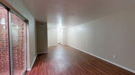 This single-floor unit offers a well-organized and functional layout highlighted by rich, warm-toned hardwood-style flooring that flows seamlessly throughout every room, creating a cohesive and inviting atmosphere. The open living area is generously proportioned, featuring neutral-toned walls, clean white baseboards, and ceiling vents that ensure comfortable climate control. A sliding glass door leads to an outdoor area, allowing natural light to brighten the space and providing pleasant views of surrounding greenery.

The kitchen is efficiently designed with granite-patterned countertops, a double-basin stainless steel sink, white cabinetry providing ample storage, and a dishwasher, making it both practical and clean in appearance.

The bedrooms are comfortably sized, each featuring ceiling fans with lighting, large windows that frame lush outdoor tree views, and access to dedicated walk-in closets with shelving — offering excellent storage solutions. The adjacency of the bathroom to the bedroom area enhances convenience.

The full bathroom includes a wood-toned vanity with a white countertop, a wall mirror, and a full tub-shower combination with white tile surround, maintaining a clean and functional aesthetic throughout. Overall, this unit presents a practical and comfortable living environment with consistent finishes and a warm, neutral palette.