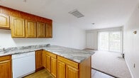 This efficient and thoughtfully designed 1-bedroom, 1-bathroom single-floor residence offers a functional layout across a compact yet comfortable footprint. The kitchen is a standout feature, boasting warm honey-toned wood cabinetry extending to the ceiling, stone-patterned countertops, and a peninsula that opens toward the living area — ideal for both cooking and casual dining. A skylight overhead bathes the kitchen in natural light, while hardwood-style flooring adds a clean, polished look. White appliances, including a dishwasher, range, microwave, and refrigerator, are included. The open living area flows naturally from the kitchen and features plush carpeting, creating a comfortable and inviting atmosphere. Large sliding glass doors with vertical blinds allow generous natural light and provide access to an outdoor area. The bedroom is generously proportioned, with soft carpeting, a built-in closet, and its own sliding glass door offering additional natural light and outdoor views. The bathroom features white square tile walls and flooring, a vanity with mirror cabinet, and a clean, straightforward design. A hallway connects the rooms, completing this well-organized and practical floor plan.