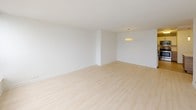 This single-floor unit presents a clean, minimalist design throughout, characterized by crisp white walls, light hardwood flooring, and an abundance of natural light. The layout, as revealed by the 3D floor plan, is well-organized and spacious, offering multiple rooms arranged for comfortable living.

The living areas are notably bright, benefiting from large floor-to-ceiling windows that frame sweeping high-rise city views, filling the rooms with daylight and providing a strong connection to the surrounding urban landscape. The light hardwood floors run consistently through the main living spaces and bedrooms, contributing to a cohesive, airy aesthetic.

The kitchen is thoughtfully designed with white cabinetry, wood-toned lower cabinets, light countertops, and stainless steel appliances including a range, built-in microwave, and dishwasher. Tile flooring in the kitchen provides a practical transition from the living areas.

Two bathrooms serve the unit, each featuring a soaking tub with an overhead shower, neutral beige tile surrounds, chrome fixtures, and warm-toned tile flooring. The bedrooms are generously proportioned, each benefiting from corner or multi-window configurations that maximize both light and views. Overall, the space conveys a modern, understated elegance suited for urban living.