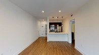 This single-floor residence offers a well-designed layout that balances open communal spaces with private retreats. The living area is generously proportioned, featuring warm hardwood-style flooring, recessed lighting, and crisp white walls that create a bright, clean atmosphere. A striking textured stone accent wall adds visual interest near the sliding door, which opens to a balcony and allows natural light to fill the space.

The kitchen is thoughtfully designed with dark espresso cabinetry, a subway tile backsplash, and a full suite of stainless steel appliances including a gas range, microwave, and refrigerator. A peninsula with pendant lighting provides a natural transition between the kitchen and living area, while built-in open shelving near the entry adds convenient storage.

The bedroom features dark hardwood-style flooring, a cool-toned accent wall, and a window with outdoor views of lush surroundings. An en-suite bathroom connects directly to the bedroom and includes a tub and shower combination with clean white tile surround. A second bathroom, also featuring a tub/shower combo, provides additional convenience. Throughout the unit, consistent flooring, neutral tones, and modern fixtures contribute to a cohesive and contemporary aesthetic.