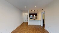 This single-floor residence offers a well-designed layout that balances open communal spaces with private retreats. The living area is generously proportioned, featuring warm hardwood-style flooring, recessed lighting, and crisp white walls that create a bright, clean atmosphere. A striking textured stone accent wall adds visual interest near the sliding door, which opens to a balcony and allows natural light to fill the space.

The kitchen is thoughtfully designed with dark espresso cabinetry, a subway tile backsplash, and a full suite of stainless steel appliances including a gas range, microwave, and refrigerator. A peninsula with pendant lighting provides a natural transition between the kitchen and living area, while built-in open shelving near the entry adds convenient storage.

The bedroom features dark hardwood-style flooring, a cool-toned accent wall, and a window with outdoor views of lush surroundings. An en-suite bathroom connects directly to the bedroom and includes a tub and shower combination with clean white tile surround. A second bathroom, also featuring a tub/shower combo, provides additional convenience. Throughout the unit, consistent flooring, neutral tones, and modern fixtures contribute to a cohesive and contemporary aesthetic.