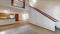 This two-story residence offers a thoughtfully laid-out interior with a blend of functional and comfortable living spaces throughout both levels. The main level centers around a generous open living area distinguished by soaring vaulted ceilings and a striking staircase with warm wood railings. A ceiling fan overhead and plush wall-to-wall carpeting contribute to a welcoming atmosphere, while the open sightlines to the upper loft-style balcony add a sense of grandeur and vertical scale.

The kitchen is well-equipped with ample warm-toned wood cabinetry, granite-style countertops, and white appliances including a refrigerator, electric range, and dishwasher. Light tile flooring ties the space together cleanly and practically.

Bedrooms are carpeted and bright, with windows framing leafy outdoor views and baseboard heating for year-round comfort. Each room offers generous proportions, and at least one bedroom features a built-in closet with bifold doors for convenient storage. The two bathrooms are finished with tile flooring, wood vanities, and tub-shower combinations.

A dedicated laundry area houses a full-size washer and dryer, adding everyday convenience. A carpeted staircase with recessed lighting connects the two floors, completing this well-organized and comfortable multi-level home.
