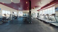 Located in Draper, Utah, this single-floor fitness center combines energetic design with comprehensive workout amenities. The entrance corridor immediately sets the tone with a bold, large-scale urban mural covering an entire wall, depicting a vivid cityscape rendered in striking reds, oranges, and blues. Geometric blue-and-charcoal patterned carpet tiles line the entryway, leading visitors into the main workout floor.

The primary exercise area features rubber flooring, floor-to-ceiling mirrors along the walls, and a dramatic deep-magenta ceiling accented by recessed lighting and ceiling fans. This space is well-stocked with cardio machines including treadmills and stair climbers, a full dumbbell rack, and cable weight machines. Large windows allow abundant natural light to fill the room.

A glass-enclosed children's play area is seamlessly integrated into the facility, featuring colorful checkerboard flooring, whimsical tree murals, bright toys, and a small table—providing a safe, cheerful space for young visitors.

A separate studio room offers an open, flexible space for spin cycling, yoga, or group fitness. Outfitted with rubber flooring, a spin bike, yoga mats, and colorful wall art, the room is bathed in natural light through oversized windows that frame sweeping views of the surrounding Utah landscape and distant mountains.