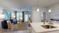 This single-story residence offers a thoughtfully designed open-concept floor plan that seamlessly connects the kitchen, dining, and living areas. The kitchen is outfitted with white shaker cabinetry, quartz countertops, stainless steel appliances, and a central island with pendant lighting and bar seating—ideal for both cooking and casual entertaining. Light wood-look flooring extends throughout the main living areas, contributing to a clean, cohesive aesthetic. The dining area accommodates a glass-top table with seating for four, accented by a decorative mirror and gallery wall. The living room features large windows that allow ample natural light, complemented by a ceiling fan and neutral gray walls.

The primary bedroom is carpeted and generously sized, with natural light filtering through blinds and drape-framed windows. A second bedroom also features carpet, a ceiling fan, and window treatments. The bathroom includes a glass-enclosed shower, light wood-look flooring, white cabinetry, and a quartz vanity top. A dedicated laundry area houses a full-size washer and dryer with wire shelving for storage. Overall, the space presents a modern, neutral palette throughout.