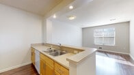 This single-story residence in El Cerrito, California offers a practical and well-organized layout with a clean, neutral aesthetic throughout. The open-concept kitchen serves as a central hub, featuring warm honey-toned cabinetry, light stone-finish countertops, a double stainless steel sink, and a full suite of white appliances including an electric range, microwave, refrigerator, and dishwasher. A peninsula counter with a raised bar edge connects the kitchen to the adjacent living area, enhancing the sense of openness. Recessed and flush-mount lighting illuminate the kitchen and transition spaces effectively.

The living area benefits from rich hardwood-style flooring that extends through the main spaces, creating a cohesive and inviting atmosphere. Natural light filters in through blinds-fitted windows. The bedrooms are carpeted for comfort and each includes closet storage, with one featuring a spacious walk-in closet. Windows in the bedrooms admit ample natural light, further brightening these restful spaces.

The bathrooms are well-appointed, with one featuring a full tub-shower combination with white tile surround, and another offering a vanity with a large mirror, warm overhead lighting, and matching cabinetry. Both maintain a clean, functional design consistent with the rest of the residence.