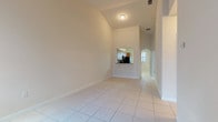 Located at 677 NE 35 Ave in Homestead, Florida, Unit 203 is a single-floor residence that offers a well-designed layout with a clean, neutral aesthetic throughout. The living area is immediately impressive, featuring soaring vaulted ceilings that lend an open, airy feel to the space. Light-toned ceramic tile flooring runs consistently throughout the unit, contributing to a cohesive and easy-to-maintain interior. Natural light flows in through windows fitted with horizontal blinds, brightening each room effectively.

The kitchen is functionally equipped with warm-toned wood cabinetry extending to the ceiling for ample storage, granite-style countertops, a dark tile backsplash, and a full suite of black appliances including a refrigerator, electric range, over-the-range microwave, and dishwasher. A pass-through window connects the kitchen to the living area, enhancing the open feel of the common spaces.

The bedrooms are comfortably sized with vaulted or elevated ceilings and windows that allow natural light to enter. The unit includes two bathrooms, each featuring tile flooring, a wood-toned vanity with white countertop, and neutral wall tiling. One bathroom includes a full tub-shower combination, while the other serves as a convenient half or secondary bath. The overall ambiance is bright, clean, and move-in ready.