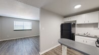 This 1-bedroom, 1-bathroom unit offers a thoughtfully designed single-floor layout that maximizes every square foot. The open living area features wood-look luxury vinyl plank flooring, neutral gray walls, and a textured ceiling, creating a clean and contemporary atmosphere. Natural light enters through a large window fitted with blinds, brightening the space. A dedicated entry door leads directly into the living area, providing a welcoming transition into the home.

The kitchen is efficiently arranged with white cabinetry, a granite-style countertop, a gas range, a black refrigerator, and a stainless steel sink. A peninsula breakfast bar adds additional counter space and visually connects the kitchen to the living area, making it ideal for both meal prep and casual dining.

The bedroom is carpeted for comfort and features a ceiling fan with a light fixture, a window with blinds for natural light and privacy, and access to a dedicated closet for storage.

The bathroom is finished with a white vanity featuring a dark countertop, a full tub-shower combo, and matching wood-look flooring that ties the space together cohesively. Clean white fixtures and chrome hardware complete the functional and tidy design. Overall, the unit presents a consistent, neutral palette well-suited for a variety of interior styles.