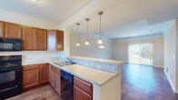 Located at 1300 Community Way in Lancaster, Ohio, this two-story home offers a well-designed layout that balances comfort and functionality. The main level centers around an open-concept kitchen and living area, where rich wood-toned cabinetry, light stone-style countertops, and a full suite of black appliances—including a range, microwave, dishwasher, and refrigerator—come together in a spacious, well-lit kitchen. A peninsula with pendant lighting provides additional prep and seating space, while hardwood-style flooring flows throughout the main level. The living area extends naturally from the kitchen, bathed in natural light from a large sliding glass door. A carpeted staircase with a clean white railing leads to the upper level, where multiple bedrooms feature vaulted ceilings, plush carpeting, and windows offering outdoor views. The primary bathroom is appointed with dual sinks, a glass-enclosed walk-in shower, and hardwood-style flooring. A secondary full bathroom includes a single vanity with wood cabinetry and a tub-shower combination. Neutral warm tones throughout create a welcoming, move-in-ready atmosphere across both floors.