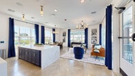 Located at 4980 Red Maple Ln in Wildwood, Florida, this single-floor open-concept space seamlessly integrates a kitchen, dining room, and living room into one cohesive and thoughtfully designed layout. The kitchen serves as a striking focal point, anchored by a large waterfall-edge quartz island with bar seating. White cabinetry lines the back wall beneath an illuminated arched alcove housing a mounted display screen, complemented by gold pendant lighting and modern fixtures. Polished concrete floors run throughout, lending the space an understated industrial elegance. The dining area features a solid wood table beneath a multi-light chandelier, surrounded by large windows dressed in bold navy curtains that flood the room with natural light and views of the surrounding neighborhood. The living room is defined by a sputnik-style chandelier overhead and floor-to-ceiling sliding glass doors that open directly to an outdoor pool and patio area, blurring the line between interior and exterior. Deep navy and cognac seating arrangements contribute to a vibrant, contemporary color palette. Abundant windows on multiple walls ensure the entire space remains bright and welcoming throughout the day.