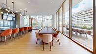 Located at 88 Bathurst Street in Toronto's vibrant King West neighbourhood, this single-floor amenity space offers a generously sized, open-concept layout designed for both social gathering and productive use. The interior is defined by dramatic floor-to-ceiling glazing that wraps along the exterior walls, flooding the space with abundant natural light and framing panoramic views of the surrounding Toronto skyline and neighbourhood rooftops. Light hardwood flooring runs throughout, contributing to a warm, contemporary aesthetic.

The space is thoughtfully divided into distinct functional zones. A casual lounge area anchors one section, featuring a large modular sectional sofa, patterned area rug, and mid-century modern accent chairs, complemented by a sculptural multi-bulb pendant chandelier overhead. Adjacent to this is a more intimate seating arrangement with leather lounge chairs and low side tables positioned directly beside the expansive glazed facade. A formal dining and meeting area accommodates a large rectangular conference table surrounded by upholstered chairs, ideal for group gatherings or events. A separate casual dining zone with round tables and mixed seating adds further flexibility.

Glass-partitioned rooms with sleek black steel frames provide semi-private enclosures within the open layout. Direct access to a spacious outdoor terrace extends the usable area and enhances the connection to the cityscape beyond.