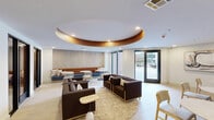 Located at 1220 South Ave in Plainfield, NJ, this thoughtfully designed communal lounge space offers a sophisticated and welcoming environment across a single, generously proportioned floor. The space is immediately distinguished by its eye-catching circular ceiling feature, finished in warm copper tones and inset with recessed lighting, which anchors the central lounge area and adds a bold architectural focal point.

The main lounge area is furnished with plush, dark upholstered armchairs and sofas arranged on a patterned area rug over light hardwood-style flooring, creating an inviting setting for relaxed gatherings or informal meetings. A built-in banquette seating area along one wall features rich caramel leather cushions paired with a navy blue base, complemented by round white tables and light wood chairs — ideal for small group conversations or casual dining.

The rear wall showcases a textured sculptural panel with geometric relief detailing, adding depth and artistic interest to the space. Abstract artwork adorns the walls, contributing to the contemporary aesthetic. Large windows and glass doors allow natural light to fill the interior, while offering views to the outdoors.

A series of glass-partitioned private rooms with black-framed doors line one side of the space, providing enclosed areas suitable for focused work or small meetings. The overall ambiance balances modern design with warm, comfortable furnishings, making this a versatile and refined communal destination.