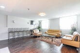 Located at 2770 Aquitaine Ave in Mississauga, Ontario, this single-floor space offers a comfortable and functional layout designed for both relaxation and social interaction. The main living area is bright and welcoming, featuring rich hardwood flooring throughout, a textured ceiling, and large windows dressed with vertical blinds that allow generous natural light to pour in while offering views of the surrounding greenery.

The open-concept design connects the living area seamlessly to a clean, modern kitchen outfitted with white cabinetry, stainless steel appliances including a refrigerator and dishwasher, and a built-in microwave — providing a fully functional cooking space. A bar-style seating area with high chairs and a wall-mounted television adds a casual entertainment element to the layout.

A separate multi-purpose room serves as a dining and lounge area, furnished with multiple round tables and chairs, making it well-suited for group gatherings or casual meetings. Warm wall sconces and flush-mount ceiling fixtures provide soft, layered lighting throughout. Additional nook seating near windowed areas offers quiet spots with pleasant outdoor views. The consistent use of hardwood flooring, warm-toned wood rail accents, and neutral walls creates a cohesive, inviting ambiance across the entire space.
