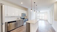 Located at 535 Main St in Nashville's 37206 zip code, this well-appointed 1-bedroom, 1-bathroom residence offers a thoughtfully designed single-level layout with modern finishes throughout. The open-concept kitchen and living area serves as the heart of the home, showcasing sleek white upper cabinetry, wood-toned lower cabinets, and a classic subway tile backsplash. A full suite of stainless steel appliances — including a refrigerator, range, microwave, and dishwasher — complements the light quartz countertops. A kitchen island with built-in shelving provides additional prep and storage space, while a trio of globe pendant lights on red cords adds a distinctive design touch. The adjoining living area features warm hardwood-style flooring, a ceiling fan, and generous natural light from large windows. The bedroom offers plush carpeting, a bright window with views of the Nashville skyline, and a dedicated closet for storage. The bathroom is well-equipped with a granite-topped vanity, wood-toned cabinetry, a soaking tub, and a separate glass-enclosed shower, all finished with clean white tile and hardwood-style flooring.
