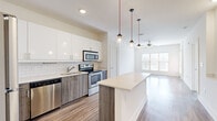 Located at 535 Main St in Nashville's 37206 zip code, this well-appointed 1-bedroom, 1-bathroom residence offers a thoughtfully designed single-level layout with modern finishes throughout. The open-concept kitchen and living area serves as the heart of the home, showcasing sleek white upper cabinetry, wood-toned lower cabinets, and a classic subway tile backsplash. A full suite of stainless steel appliances — including a refrigerator, range, microwave, and dishwasher — complements the light quartz countertops. A kitchen island with built-in shelving provides additional prep and storage space, while a trio of globe pendant lights on red cords adds a distinctive design touch. The adjoining living area features warm hardwood-style flooring, a ceiling fan, and generous natural light from large windows. The bedroom offers plush carpeting, a bright window with views of the Nashville skyline, and a dedicated closet for storage. The bathroom is well-equipped with a granite-topped vanity, wood-toned cabinetry, a soaking tub, and a separate glass-enclosed shower, all finished with clean white tile and hardwood-style flooring.