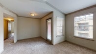 This single-story residence offers a thoughtfully arranged layout with multiple rooms designed for comfortable everyday living. The living area serves as the welcoming centerpiece of the home, featuring a vaulted ceiling that enhances the sense of openness and volume. Multiple windows fitted with horizontal blinds allow natural light to fill the space, while plush carpeting adds warmth underfoot. A front entry door provides direct access to this bright, airy room.

The bedrooms continue the carpeted flooring and neutral wall tones found throughout the home. One bedroom includes a ceiling fan with a light fixture, a closet with a rod and shelving system, and a window overlooking the exterior. Another bedroom connects directly to the full bathroom, offering added convenience. Crown molding detailing is present in select rooms, adding a refined architectural touch.

The kitchen is efficiently designed with warm wood-toned cabinetry, dark granite-style countertops, and wood-look flooring. White appliances including a range, over-the-range microwave, and refrigerator are all included. Ample upper and lower cabinet storage lines both sides of the kitchen corridor.

The bathroom features wood-look flooring, a tub-shower combination with tiled surround, a toilet, and a vanity with a granite-style countertop, undermount sink, and a large mirror.