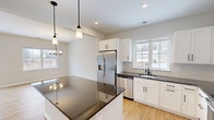 Located at 100 Ryefield Hollow Dr in Bloomfield, CT, this two-story home offers four bedrooms and three bathrooms across a well-organized layout. The main floor features an open-concept kitchen and dining area bathed in natural light from large windows. The kitchen is outfitted with crisp white shaker cabinets, dark granite countertops, a subway tile backsplash, stainless steel appliances, and a central island with pendant lighting overhead. The adjoining dining area continues the light hardwood flooring and is accented by a modern chandelier. A hallway connects the main living areas, with a bathroom conveniently accessible on this level. The attached garage provides practical storage and parking space. Upstairs, the spacious primary bedroom features a tray ceiling, plush carpeting, and a wide window offering serene wooded views. Additional bedrooms are generously sized, with hardwood-style flooring and natural light. The bathrooms are clean and functional, featuring tub-shower combinations with built-in shelving and tile flooring. Throughout the home, a neutral color palette, white panel doors with matte black hardware, and consistent finishes create a cohesive, modern aesthetic. The upper floor also includes closets and a utility room, ensuring ample storage throughout.