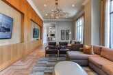 Located at 3499 Durden Dr NE in Brookhaven, Georgia, this single-floor space showcases a refined blend of contemporary and transitional design throughout its generously proportioned layout. Striking herringbone-patterned hardwood flooring flows seamlessly from room to room, anchoring the space with warmth and visual continuity.

The living areas are defined by soaring ceilings and expansive floor-to-ceiling windows that flood the interiors with abundant natural light while framing views of the surrounding greenery. Multiple seating zones are thoughtfully arranged, featuring sectional sofas, tufted leather chairs, and sculptural accent pieces that contribute to the space's curated aesthetic.

A wide, elegant corridor connects the various areas, highlighted by a coffered ceiling medallion, a decorative chandelier, and textured wall treatments that add depth and sophistication. An arched entryway leads to an intimate dining area, adding architectural character to the layout.

The kitchenette area is outfitted with white shaker cabinetry, granite countertops, stainless steel appliances including a wine cooler and built-in microwave, and a distinctive three-dimensional tile feature wall with dual mounted flat-screen televisions. This well-equipped space serves both functional and entertainment purposes, making it a versatile hub within the overall floor plan.