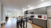 This thoughtfully designed 2-bedroom, 2-bathroom residence offers a modern, open-concept layout that seamlessly connects the kitchen, dining, and living areas. The kitchen is a standout feature, showcasing sleek gray cabinetry, white subway tile backsplash, stainless steel appliances including a range, microwave, and refrigerator, and light countertops. A high-top dining table with industrial-style stools provides a casual space for dining and entertaining. The living room is bright and welcoming, with large windows and a balcony door that invite natural light and offer views of lush greenery. Light-toned hardwood flooring flows throughout the main living areas, adding warmth to the contemporary design. The primary bedroom is a comfortable retreat, featuring plush carpeting, a closet with built-in shelving and hanging rods, and a window overlooking tree-lined surroundings. The second bedroom similarly offers carpeted flooring, natural light, and a dedicated closet. Both bathrooms are finished with wood-look flooring, white tub-shower combinations, and vanities with white countertops and gray cabinetry. A spacious walk-in closet with wire shelving provides ample additional storage. Recessed lighting throughout enhances the clean, modern aesthetic of this well-appointed residence.