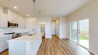 Located at 2230 Peregrine Dr in Brighton, Colorado, this two-story, three-bedroom, three-bathroom home offers a clean, modern aesthetic with thoughtfully designed living spaces spread across two floors. The main level features an open-concept kitchen and living area finished with warm wood-look flooring throughout. The kitchen is highlighted by a sleek white island with a undermount sink, pendant lighting with brushed gold accents, crisp white cabinetry, and a dedicated pantry with built-in shelving — ideal for organized storage. Sliding glass doors connect the living area to the exterior, filling the space with natural light. The upper floor hosts all three bedrooms, including a generously sized primary bedroom with plush carpet, a ceiling fan, and a walk-in closet outfitted with dual hanging rods. Additional bedrooms feature wood-look flooring and multiple windows that bring in ample natural light. Three full bathrooms serve the home, one featuring a tub-shower combination with classic white subway tile surround. A dedicated laundry area with side-by-side washer and dryer adds everyday convenience. Throughout, the home presents a bright, neutral palette with recessed lighting and clean white trim, creating a fresh and welcoming atmosphere.