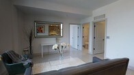 Located along the vibrant North High Street corridor in Columbus, Ohio, this single-floor unit offers a well-appointed interior designed with a clean, contemporary aesthetic. The living area serves as the central gathering space, featuring terrazzo-style flooring that adds a classic yet refined touch throughout. A gray sofa anchors the seating area, complemented by a glass coffee table that enhances the open, airy feel of the room. A sleek console table is positioned beneath a large beveled mirror, creating an elegant focal point that reflects light and adds visual depth to the space.

Neutral gray walls and crisp white trim maintain a cohesive, minimalist palette throughout the unit. Visible from the living area, a hallway leads to additional rooms, including a bathroom with white fixtures and clean tile finishes. Multiple interior doors, trimmed in white with black hardware accents, provide access to adjoining spaces, adding a subtle modern contrast to the overall design. A wall-mounted HVAC vent ensures climate comfort discreetly integrated into the architecture. The overall ambiance is calm, uncluttered, and move-in ready, well-suited for urban living in one of Columbus's most walkable and culturally rich neighborhoods.