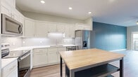 Located at 221 N Walnut Ave in Owatonna, MN, this single-floor unit offers a thoughtfully designed layout with one bedroom, two bathrooms, a dedicated closet, and an open-concept kitchen and living area. The kitchen is a standout feature, showcasing white shaker-style cabinetry, a white subway tile backsplash, light quartz countertops, a stainless steel appliance suite including a French door refrigerator, range, and over-the-range microwave, and durable light-toned luxury vinyl plank flooring. A movable island with a butcher block top adds extra prep space and flexibility. An accent wall in deep teal adds a bold pop of color to the kitchen and living area. The living room extends to a private balcony through a sliding glass door, offering views of the surrounding Owatonna cityscape. A ceiling fan with light kit enhances comfort throughout. The generously sized bedroom features plush carpet, a ceiling fan, and a large window that frames additional city views. Both bathrooms are finished with clean white tile, glass-enclosed walk-in showers, white vanity cabinetry, and tile flooring, delivering a crisp, modern aesthetic throughout.