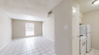 This efficient single-story unit offers a practical and functional layout across six distinct spaces. The combined living and dining area serves as the heart of the home, featuring clean white tile flooring, neutral beige walls, a textured ceiling, and a window that brings in natural light. The front entry opens directly into this open area, which provides a versatile space for both living and dining arrangements.

The galley-style kitchen is efficiently designed with white cabinetry, white tile flooring, a countertop with an integrated sink, and white appliances including a range and refrigerator. Upper and lower cabinets offer ample storage, and a pass-through counter connects the kitchen to the living area.

The bedroom is comfortably sized, finished with wall-to-wall carpet and equipped with a ceiling fan with light fixture. A window allows natural light into the room, and the space includes direct access to both a dedicated closet with built-in shelving and the full bathroom.

The bathroom features a full-size soaking tub with an overhead shower and chrome fixtures. A hallway connects the main living areas to the private bedroom wing, contributing to a logical and practical flow throughout the unit. Textured ceilings and consistent neutral tones are present throughout the space.