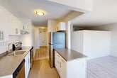 Located at 10025 115 St NW in Edmonton's vibrant Oliver neighbourhood, this single-floor unit offers a thoughtfully organized layout that maximizes every square metre of available space. The combined kitchen and living area forms the heart of the unit, where a galley-style kitchen impresses with crisp white cabinetry, granite-look countertops, a white subway tile backsplash, and a full suite of stainless steel appliances including a refrigerator, electric range, and dishwasher. A peninsula counter extends the workspace and provides a natural divide between the kitchen and the open living area. Light hardwood-style flooring runs throughout the living space, lending warmth and continuity to the interior. The living area is bright and airy, benefiting from a large sliding glass door and window that frames panoramic city views and floods the room with natural light. The bathroom is finished in a clean, modern style, featuring full-height white subway tile surrounding a soaker tub with overhead shower, complemented by granite-look countertops and sleek chrome fixtures. Neutral white walls and consistent flooring choices throughout create a cohesive, contemporary aesthetic that is both functional and inviting.