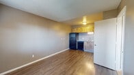 Located on E Irvington Road in Tucson, Arizona, this single-floor unit offers a practical and well-organized layout suited for comfortable everyday living. The open living area is finished with warm wood-look laminate flooring that extends throughout the main living and kitchen spaces, creating a cohesive and easy-to-maintain environment. Textured ceilings are present throughout, adding a classic residential character to each room.

The kitchen is efficiently designed along a single wall, featuring warm-toned wood upper cabinetry, a double-basin sink, a black range, a dishwasher, and a full-size black refrigerator. Under-cabinet lighting provides functional illumination for food preparation, and the layout allows for smooth workflow within the space.

The living area is open and generously proportioned, offering flexibility in furniture arrangement. A wall-mounted air conditioning unit ensures climate comfort, and a front entry door with an adjacent window allows natural light to filter into the space while providing views of the surrounding exterior.

The bedroom is carpeted for added comfort underfoot and is illuminated by a window dressed with horizontal blinds, bringing in soft natural light. A wall-mounted HVAC unit services this room independently, offering personalized temperature control. The overall neutral color palette of gray and beige tones throughout creates a clean, understated aesthetic.