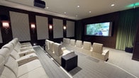 This single-level home theater is thoughtfully designed to deliver a premium cinematic experience. The room is anchored by a large projection screen at the front, providing an expansive viewing surface suited for movies, sports, and entertainment. Rows of cream-colored leather recliner seats are arranged on a tiered floor plan, ensuring unobstructed sightlines from every position. Each seat features built-in cup holders, and a sleek dark cube side table is conveniently positioned between rows for added functionality.

The walls are finished in deep, dark tones that minimize light reflection and enhance contrast on screen. Decorative acoustic panels with a textured diamond pattern are mounted symmetrically along the side walls, contributing both to the room's sound quality and its refined aesthetic. Elegant wall sconces provide warm, ambient lighting between the panels, complementing the recessed ceiling lights above.

The carpeted floor adds to the acoustic performance while reinforcing the room's sophisticated, dedicated theater atmosphere. Overall, the space balances technical functionality with upscale interior design.