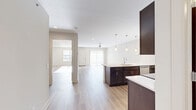 Located at 4781 Transit Rd in Depew, NY, this well-appointed one-bedroom, one-bathroom residence offers a thoughtfully designed open-concept layout with light hardwood-style flooring running throughout the entire space. The kitchen and living area flow seamlessly together, creating a bright and functional great room. The kitchen is a standout feature, showcasing rich dark-espresso cabinetry, light quartz countertops, a large peninsula with an undermount sink, stainless steel appliances including a refrigerator, range, and built-in microwave, and elegant pendant lighting overhead. The spacious living room receives generous natural light through sliding glass doors and features a ceiling fan for added comfort. The generously sized primary bedroom offers natural light through large windows, with warm light streaming across the hardwood-style floors. The full bathroom is clean and modern, featuring a glass-enclosed shower and hardwood-style flooring. Two closets provide ample storage, including a walk-in closet outfitted with wire shelving. A dedicated utility room rounds out the floor plan. The overall ambiance is fresh, modern, and move-in ready, with a neutral color palette that complements the contemporary finishes throughout.