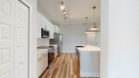 Located in Melbourne, FL, this two-bedroom, two-bathroom two-story home offers a thoughtfully designed layout across two levels. The ground floor is dedicated to a spacious garage with polished concrete floors and automated door access, providing generous storage and parking space. The main living level encompasses the bulk of the home, featuring an open-plan dining room, kitchen, and living area bathed in natural light. The kitchen is a standout, showcasing white shaker cabinetry, subway tile backsplash, stainless steel appliances, a large quartz-topped island with an undermount sink, and stylish brushed gold pendant lighting with coordinating track lighting overhead. Warm wood-look luxury vinyl plank flooring flows throughout the main living areas and bedrooms, creating a cohesive and modern aesthetic. The primary bedroom is generously proportioned with a ceiling fan and natural light from windows with blinds, complemented by a well-organized walk-in closet featuring built-in shelving and hanging systems. The bathrooms are elegantly appointed, with one featuring a navy vanity with gold hardware, quartz countertops, large-format tile in the walk-in shower, and wood-look flooring. Additional conveniences include a pantry, hallway, laundry room, and two staircases connecting the levels.