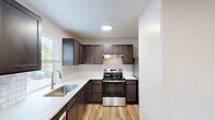 Located at 2948 W Powell Blvd in Gresham, Oregon, this single-floor, three-bedroom, two-bathroom home offers a well-organized layout with a practical mix of comfort and modern updates. The open living room is a standout, featuring warm wood-look flooring, a sleek electric fireplace with a classic white mantel, and a sliding glass door that opens to a private balcony, bringing in natural light and outdoor views. An in-unit laundry area is conveniently tucked nearby. The kitchen is thoughtfully updated with rich dark-stained cabinetry, white subway tile backsplash, light quartz countertops, stainless steel appliances including a range and dishwasher, and a stainless undermount sink positioned beneath a window overlooking greenery. The three bedrooms feature plush carpet flooring and windows that allow natural light to filter in. The primary bedroom includes direct access to a private bathroom finished with subway tile, a vanity with quartz countertops, and wood-look flooring. The second bathroom offers a full tub-shower combination. Two hallways connect the space efficiently. Neutral tones and clean finishes throughout give the home a fresh, move-in-ready feel.