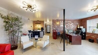 The communal spaces of Eastern Lofts Apartment Homes showcase a distinctive industrial-chic aesthetic that balances character with practicality. The leasing office serves as the welcoming centerpiece, featuring exposed brick walls, an eye-catching pipe-and-cage chandelier, and polished concrete floors. A branded reception desk anchors one side of the room, while a seating area with sleek white armchairs and a glass coffee table creates an inviting lounge atmosphere. A small kitchenette with dark cabinetry and compact appliances lines the back wall, adding convenience for staff and visitors alike.

Adjacent spaces extend the welcoming atmosphere. A casual lounge area offers bar-height tables, stools, and cozy seating arrangements bathed in natural light from street-facing windows. A bold red leather sofa sits against a textured concrete wall, adding a pop of color to one gathering zone. Stairs with dark carpet and a black metal handrail connect levels, framed by additional exposed brick detailing and a classic black entry door.

The on-site fitness center is generously proportioned, outfitted with treadmills, a stationary bike, a weight bench, and a dumbbell rack. Large mirrors, green accent walls, and patterned carpet tiles add energy to the workout space, which also benefits from natural light through multiple windows.