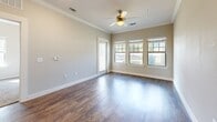 This thoughtfully designed single-story home offers a comfortable and functional layout across one bedroom, one bathroom, and a dedicated laundry area, with two closets providing ample storage. The living room makes a strong first impression with rich hardwood-style flooring, elegant crown molding, recessed lighting, and a ceiling fan. Multiple windows and a glass-paneled door flood the space with natural light while offering views of the surrounding greenery outside.

The kitchen is well-equipped, featuring dark espresso cabinetry, granite-look countertops, a double stainless steel sink, and black appliances including a range, microwave, and refrigerator. The adjacent in-unit laundry area conveniently houses a full-size washer and dryer.

The bedroom is generously proportioned, with soft carpet flooring, a ceiling fan, and multiple windows that bring in abundant natural light. A spacious walk-in closet with built-in wire shelving provides excellent storage solutions.

The bathroom maintains the cohesive design aesthetic with hardwood-style tile flooring, dark cabinetry with a granite-look vanity top, a large mirror, and a full tub-shower combination. Neutral tones throughout the home create a clean, inviting ambiance well-suited for comfortable everyday living.